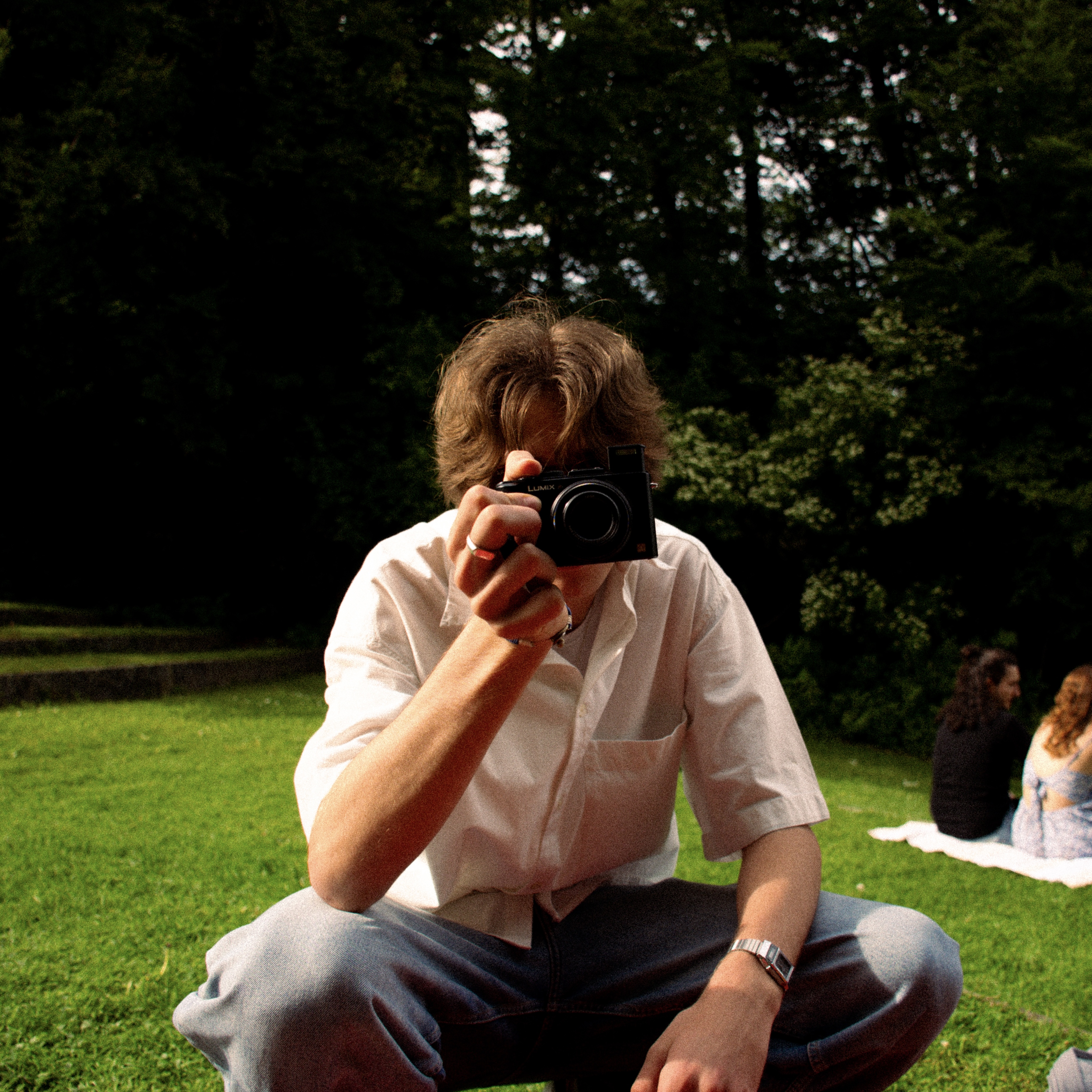 I'm on a grassy field holding a camera, with trees in the background.